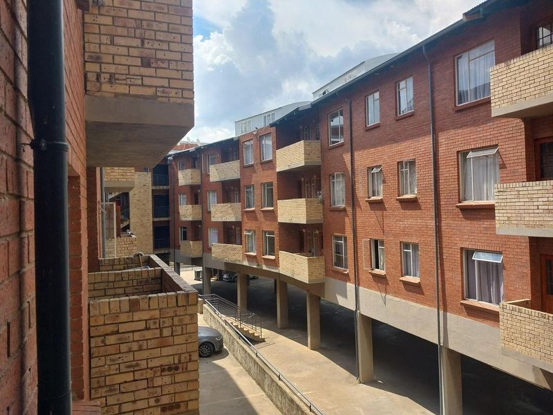 Exterior view of a multi-story apartment complex featuring face brick construction, private balconies, and a covered ground-level parking area.