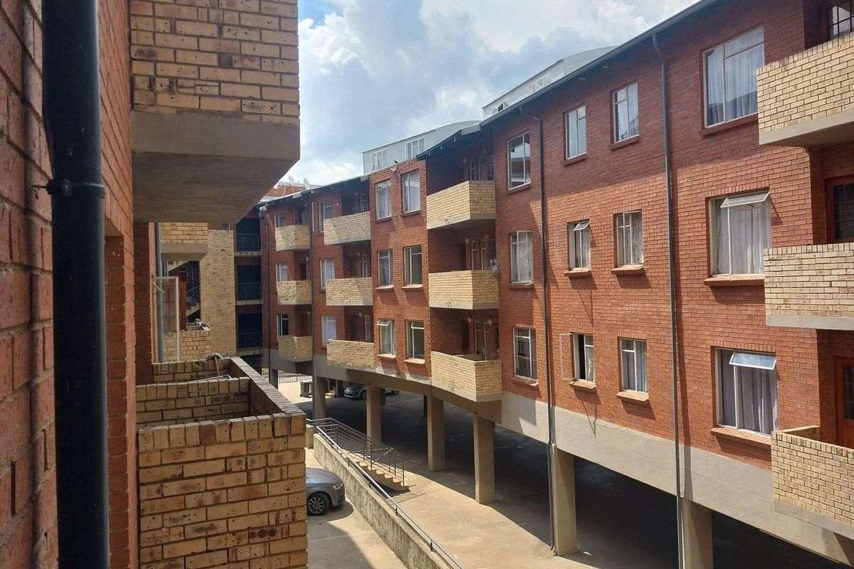 Exterior view of a multi-story apartment complex featuring face brick construction, private balconies, and a covered ground-level parking area.