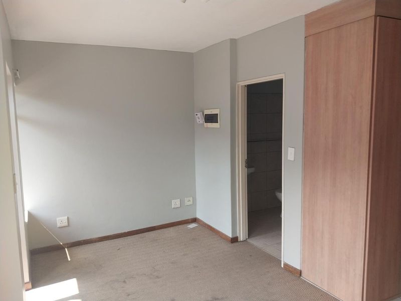 An empty bedroom featuring neutral walls, built-in wooden cupboards, and carpeted flooring, with an adjacent bathroom visible through the doorway.
