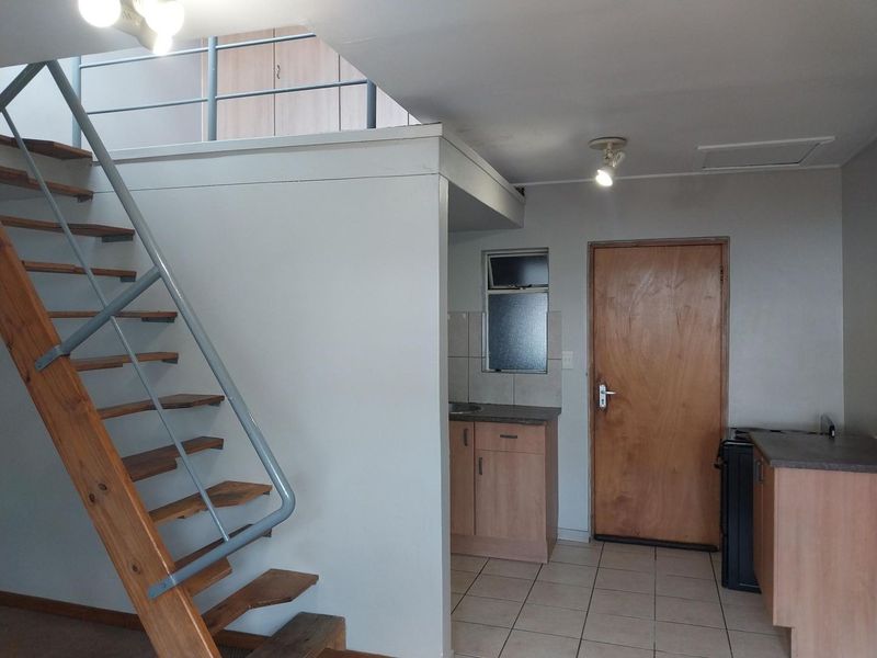 Open plan living area featuring a wooden staircase, tiled flooring, and a compact kitchen corner with built-in cabinetry.