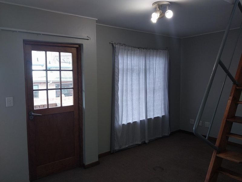 An empty living area featuring a timber framed glass door, carpeted flooring, and a wooden staircase leading to an upper level.