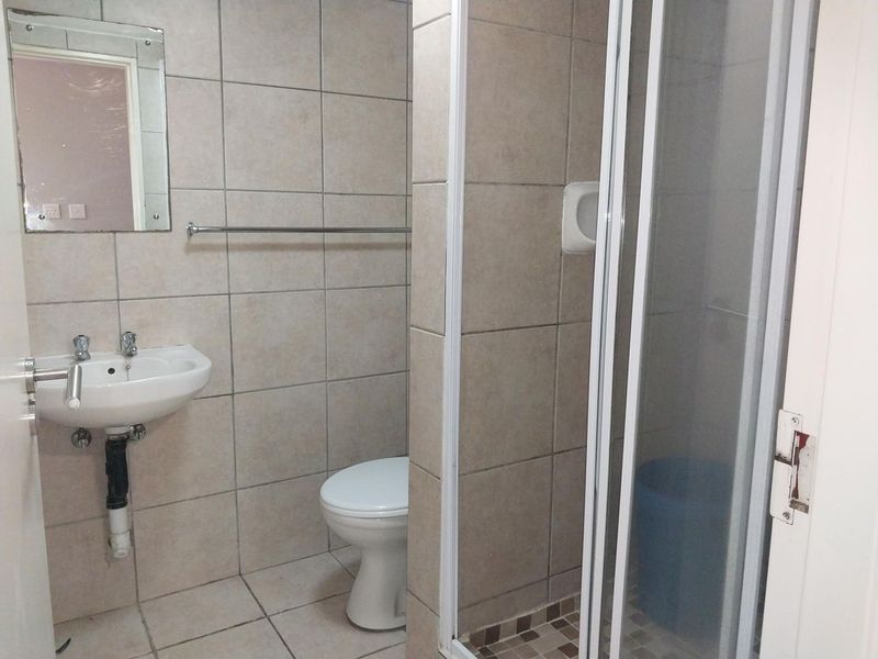 A functional bathroom featuring a shower enclosure, wall-mounted basin, and toilet with neutral wall and floor tiling.