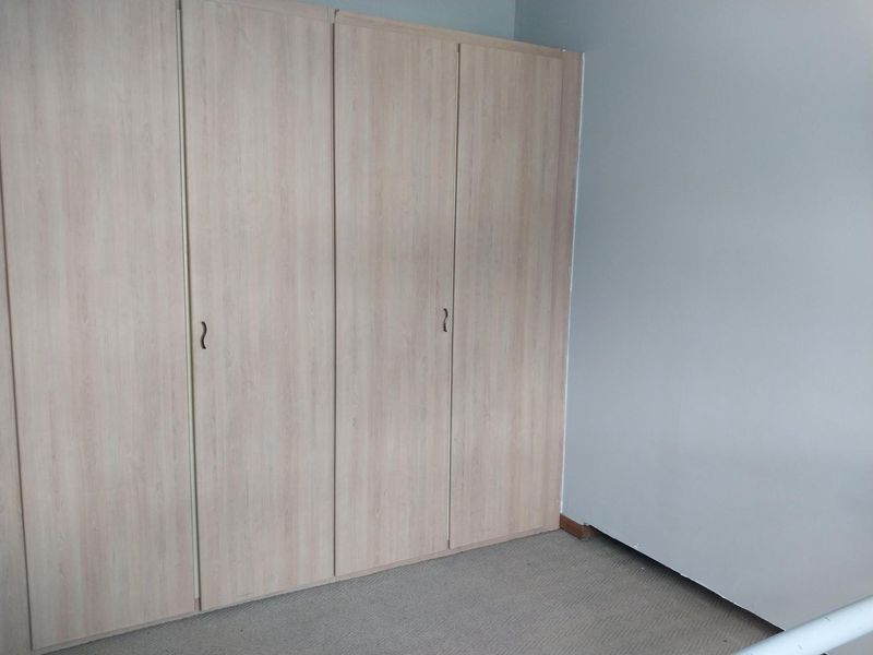 A bedroom featuring light wood-finish built-in cupboards and neutral carpeting, providing a clean and functional storage space.