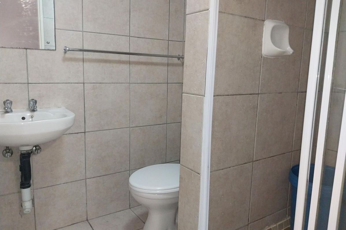 A functional bathroom featuring tiled walls and floors, a wall-mounted basin, a toilet, and a shower enclosure.