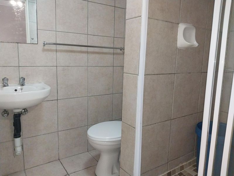 A functional bathroom featuring tiled walls and floors, a wall-mounted basin, a toilet, and a shower enclosure.