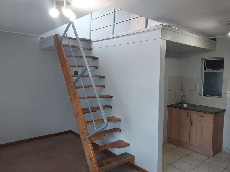 Open plan living area featuring a wooden staircase leading to a mezzanine level and a compact kitchenette with built-in cabinetry and sink.