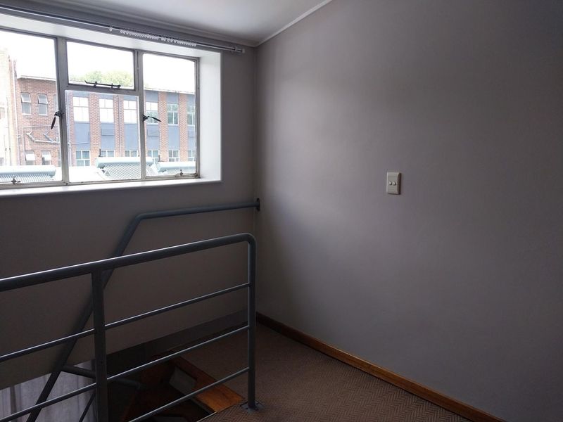 A vacant hallway area featuring carpeted flooring, a metal safety balustrade, and a window providing natural light.