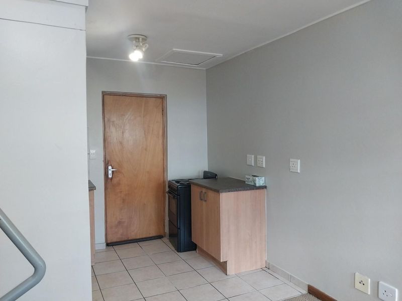 A compact kitchen area featuring built-in cabinetry, a laminate countertop, and a freestanding stove, finished with ceramic floor tiles.