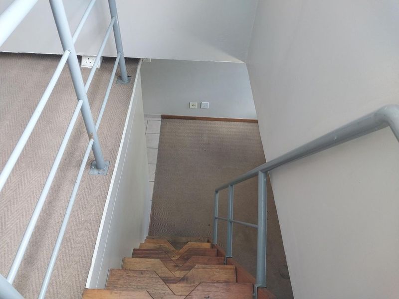 A view looking down a wooden staircase with metal handrails, leading to a carpeted landing area with neutral wall finishes.