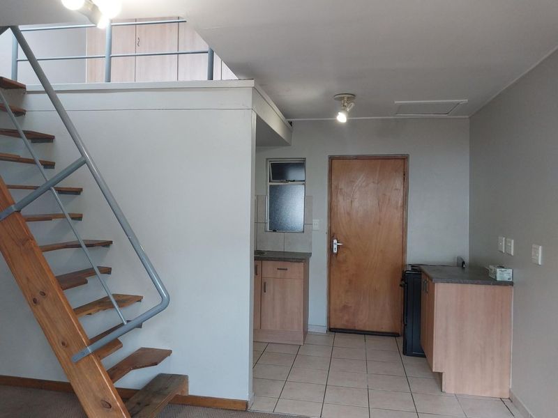 Open plan living area featuring a timber staircase leading to a loft, tiled flooring, and compact kitchen cabinetry.
