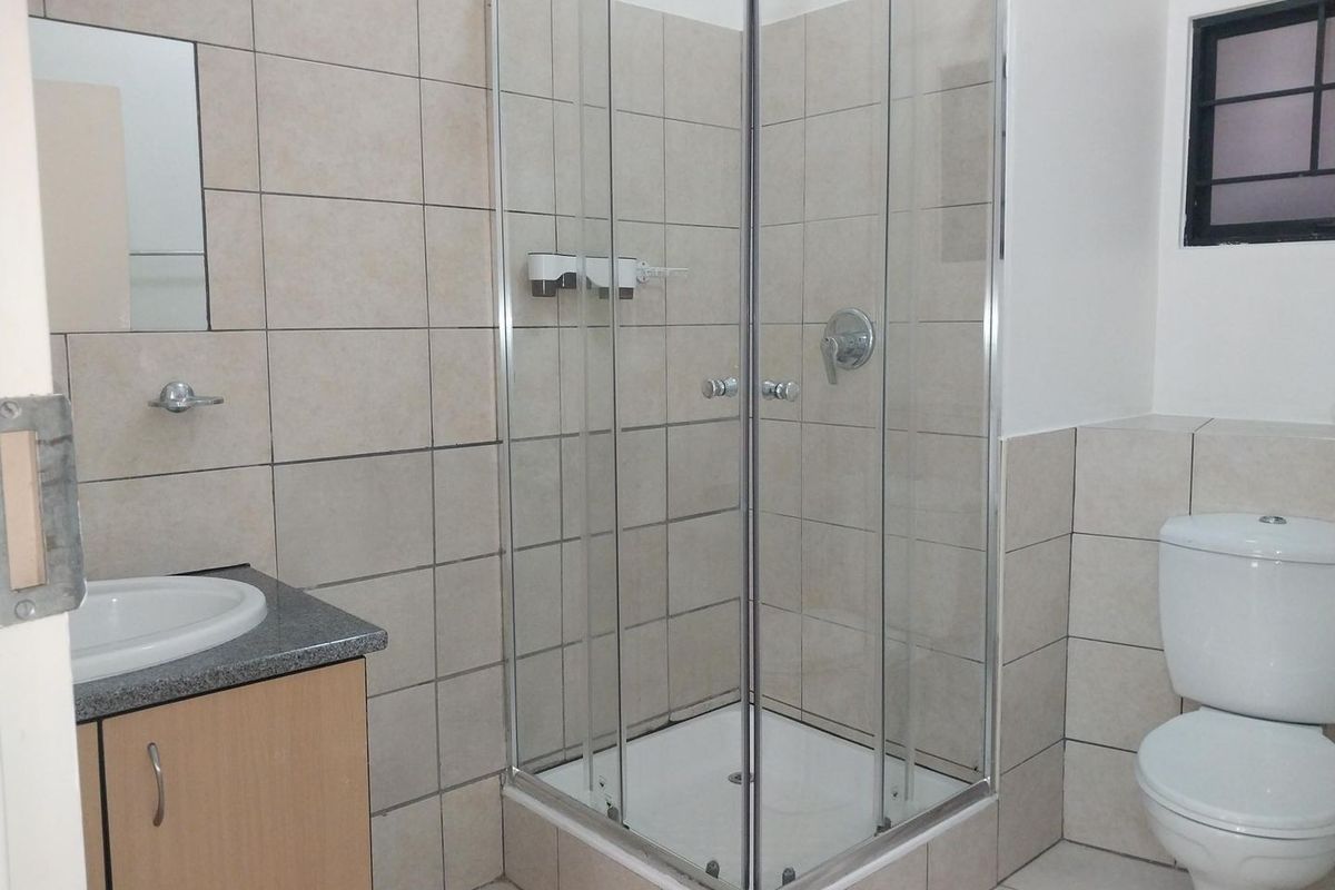 A functional bathroom featuring a corner shower enclosure, vanity cabinet with basin, and a standard toilet with neutral wall and floor tiling.