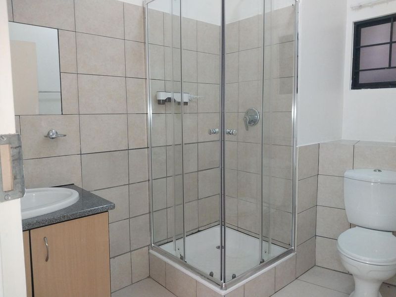 A functional bathroom featuring a corner shower enclosure, vanity cabinet with basin, and a standard toilet with neutral wall and floor tiling.