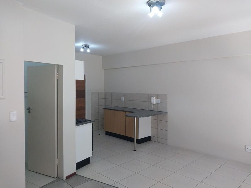 A functional, empty kitchen area featuring laminate cabinetry, stone-look countertops, tiled splashbacks, and neutral ceramic floor tiles.