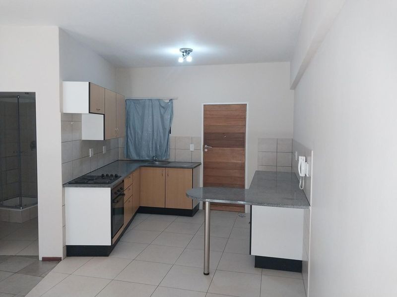 A functional kitchen featuring built-in cabinetry, laminate countertops, a breakfast bar, and integrated oven and hob, with neutral tiled flooring throughout.