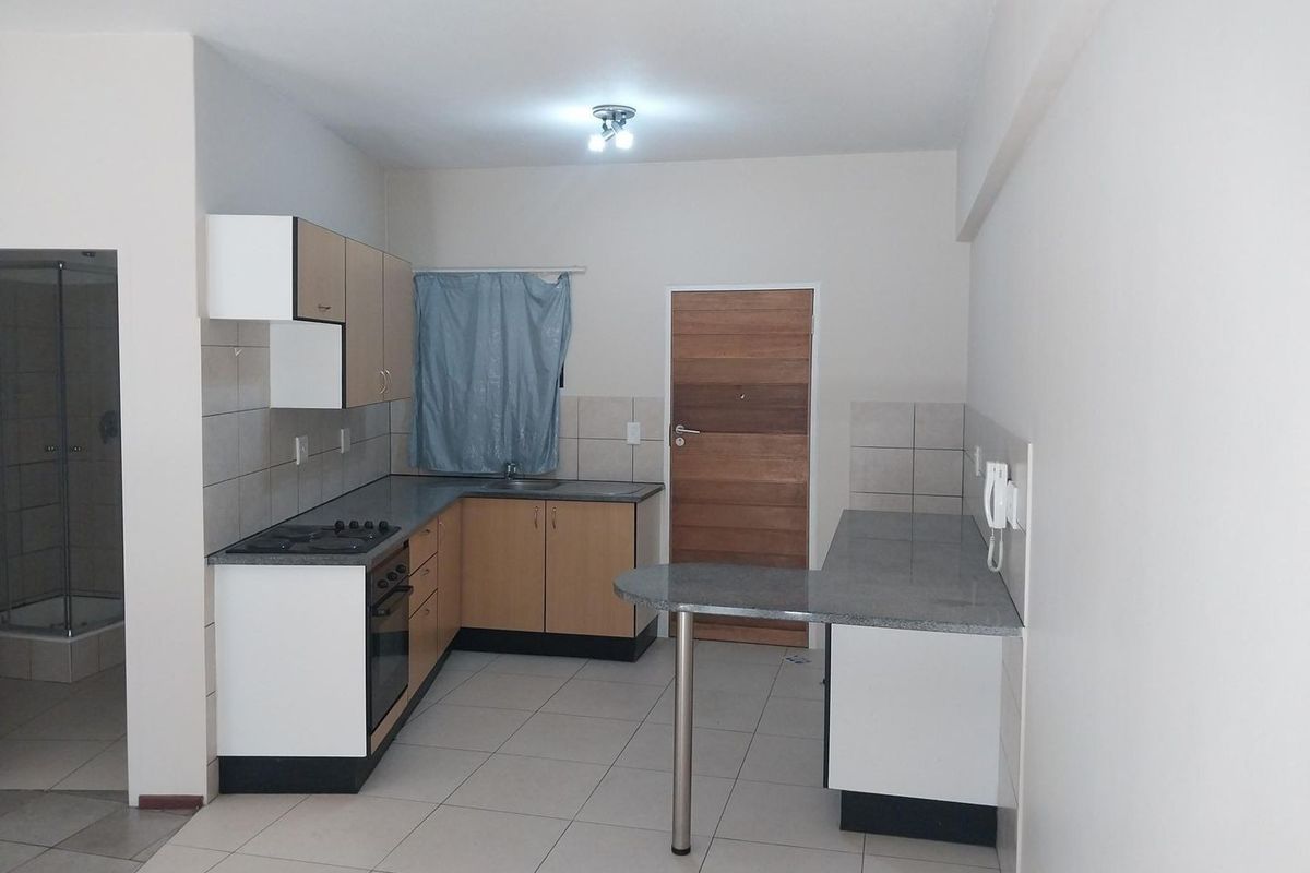 A functional kitchen featuring built-in cabinetry, laminate countertops, a breakfast bar, and integrated oven and hob, with neutral tiled flooring throughout.