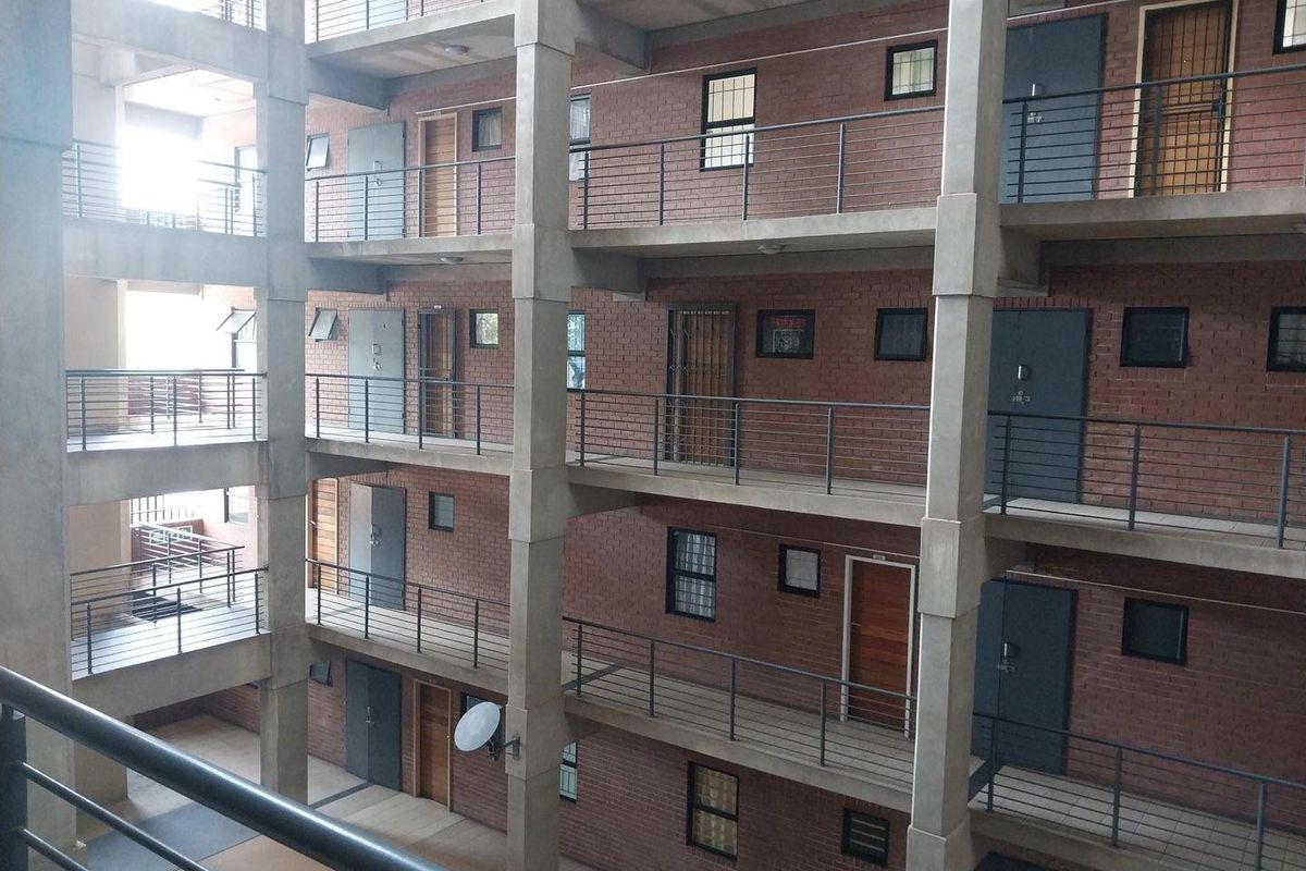 View of an apartment complex featuring exposed brick exterior, concrete structural columns, and multi-level walkways with metal security balustrades.