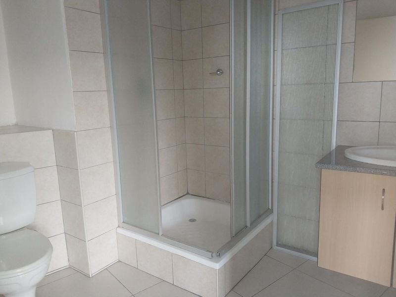 A functional bathroom featuring a corner shower enclosure, a vanity unit with a basin, and a toilet, finished with neutral wall and floor tiles.