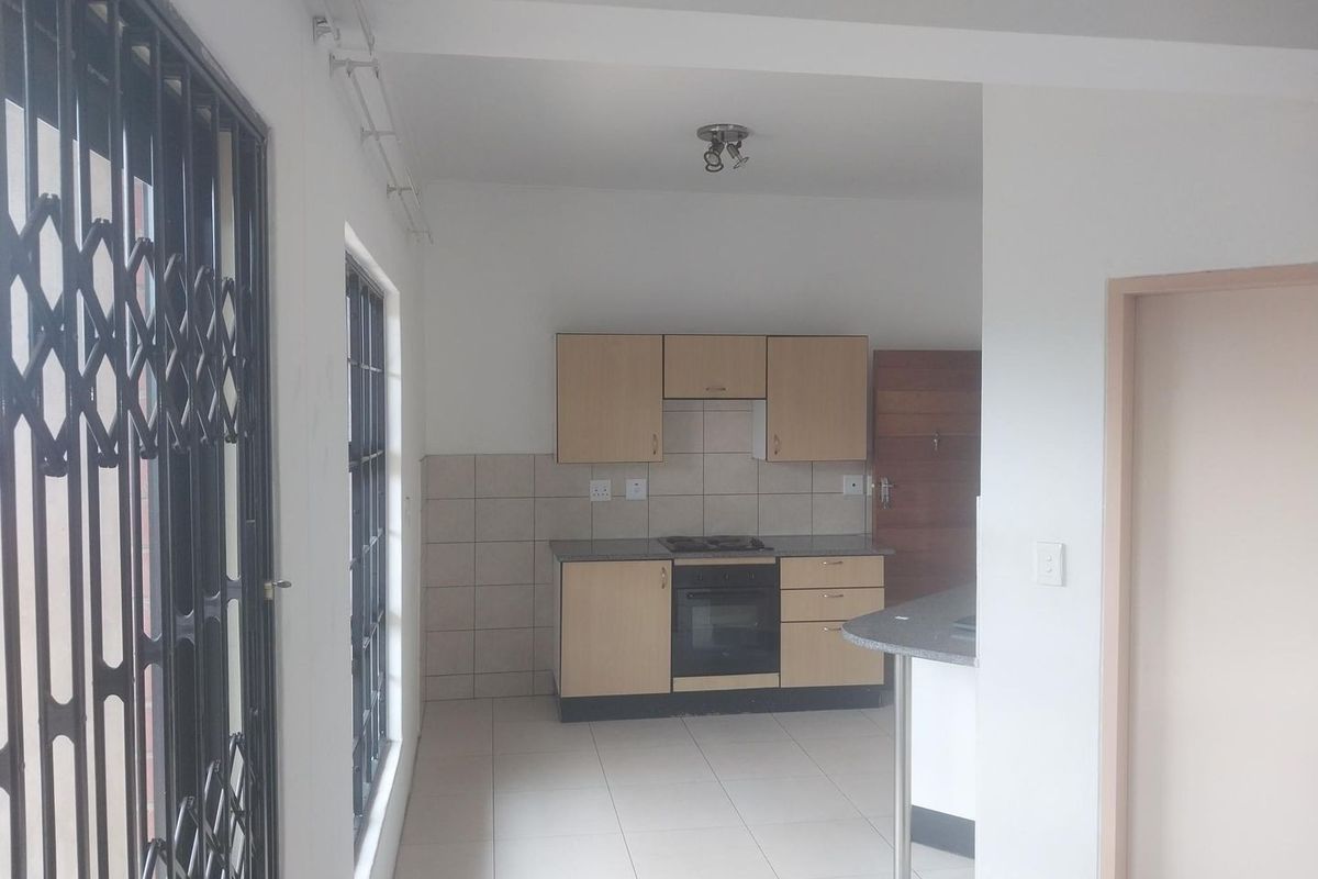 A functional kitchen featuring light wood cabinetry, a built-in oven and hob, tiled backsplash, and a breakfast counter, presented in a clean, empty space.