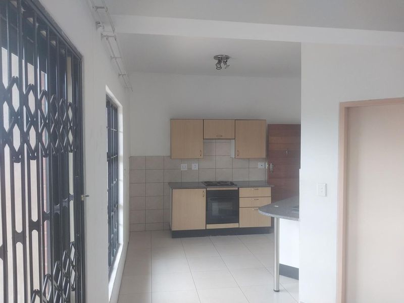 A functional kitchen featuring light wood cabinetry, a built-in oven and hob, tiled backsplash, and a breakfast counter, presented in a clean, empty space.