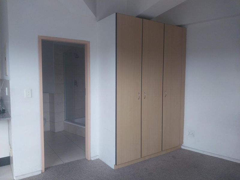 A clean, empty bedroom featuring neutral carpet flooring and a built-in wooden wardrobe, with direct access to an en-suite bathroom.
