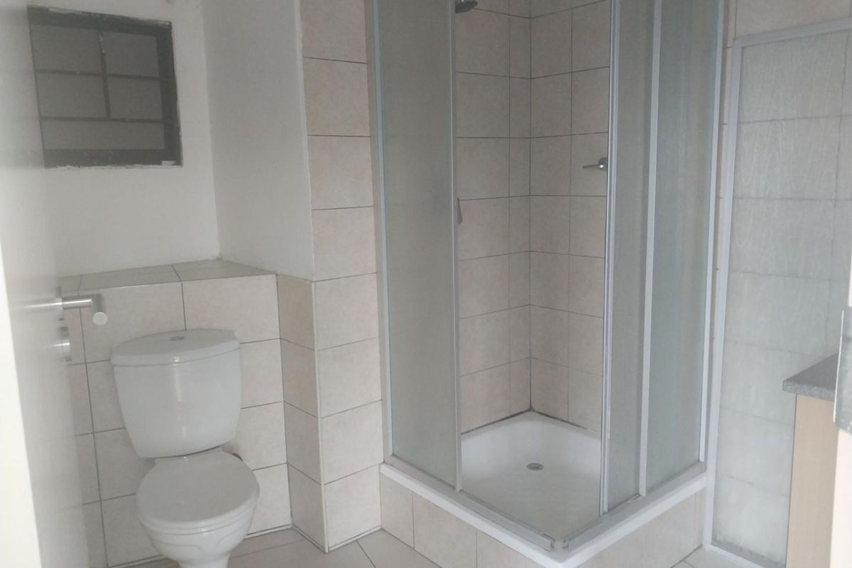 A functional bathroom featuring a corner shower enclosure, a standard toilet, and neutral wall and floor tiling.