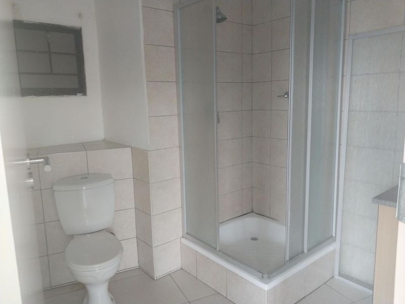 A functional bathroom featuring a corner shower enclosure, a standard toilet, and neutral wall and floor tiling.