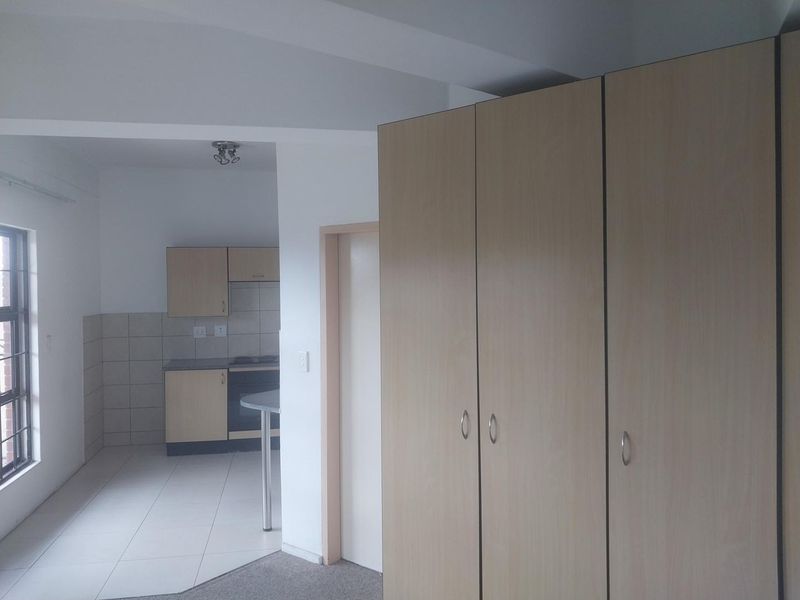 An open-plan living area featuring built-in cupboards and a functional kitchen with fitted cabinetry, oven, and hob, finished with neutral floor tiles.