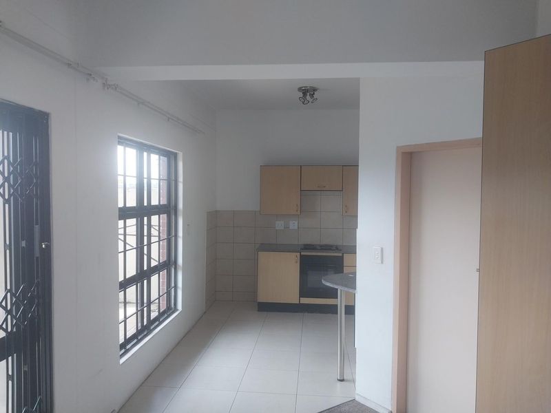 A functional, empty kitchen featuring built-in cabinetry, a tiled splashback, and a built-in oven with a hob, finished with neutral floor tiles.
