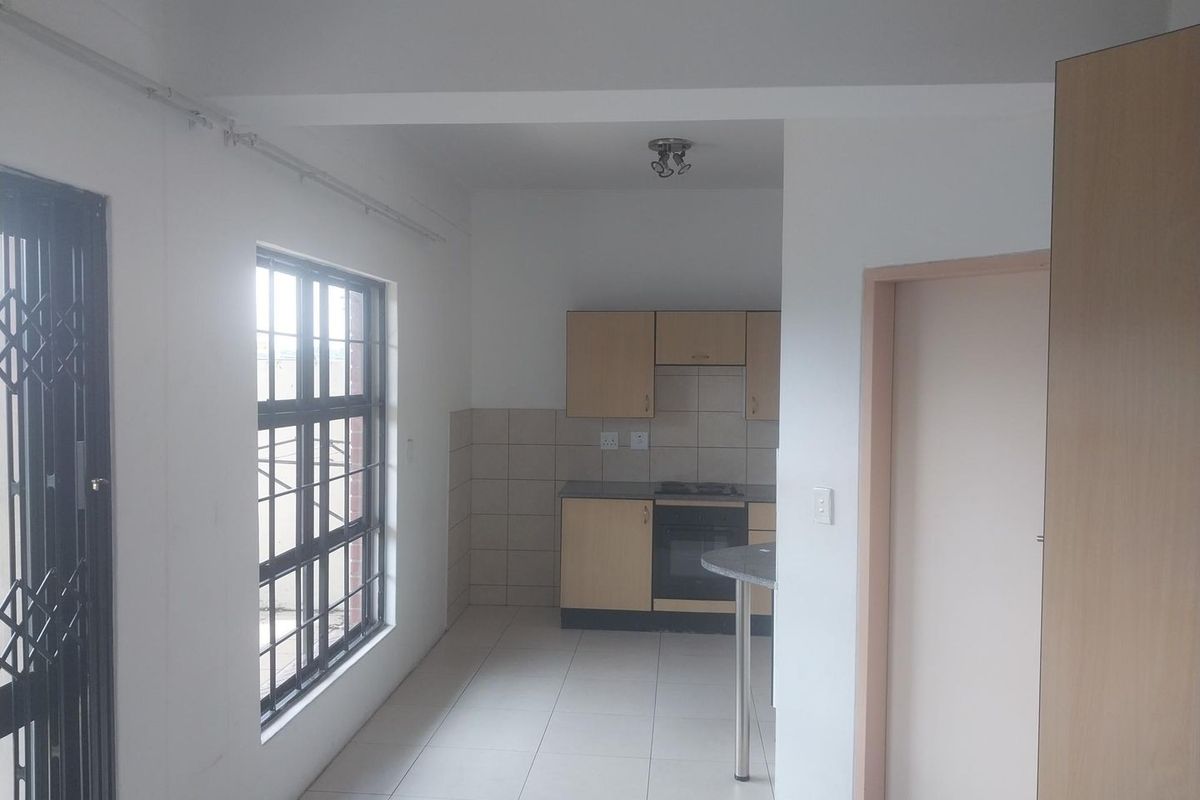 A functional, empty kitchen featuring built-in cabinetry, a tiled splashback, and a built-in oven with a hob, finished with neutral floor tiles.