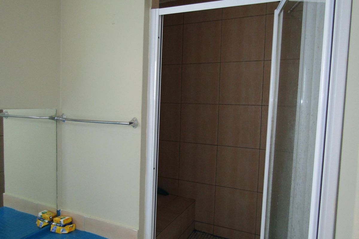 A functional bathroom featuring a walk-in shower with tiled walls and a built-in shower bench, complemented by a wall-mounted mirror and towel rail.