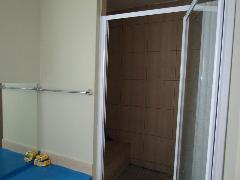 A functional bathroom featuring a walk-in shower with tiled walls and a built-in shower bench, complemented by a wall-mounted mirror and towel rail.