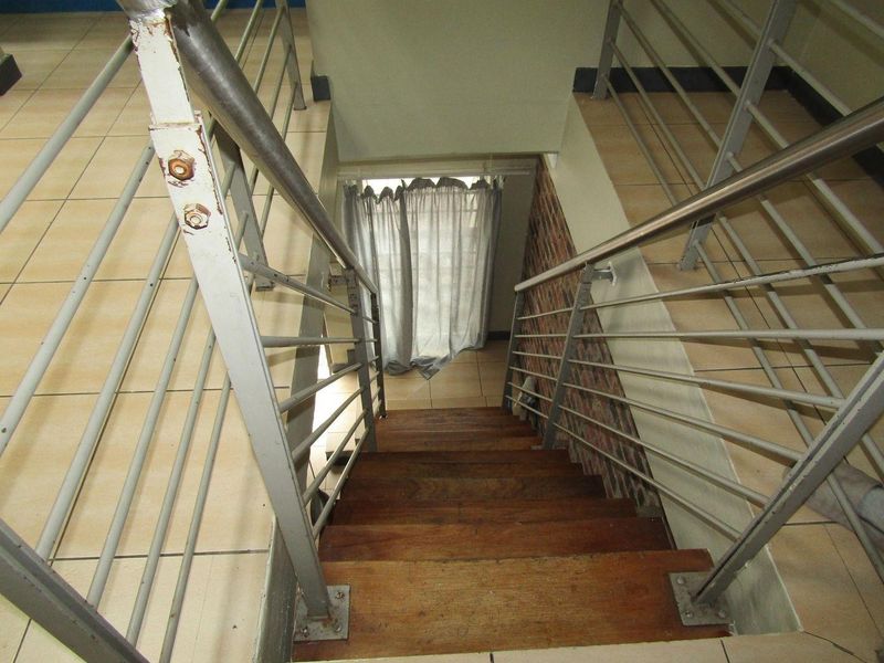 A staircase featuring wooden treads, metal balustrades, and an exposed brick wall, leading to a lower level with tiled flooring.