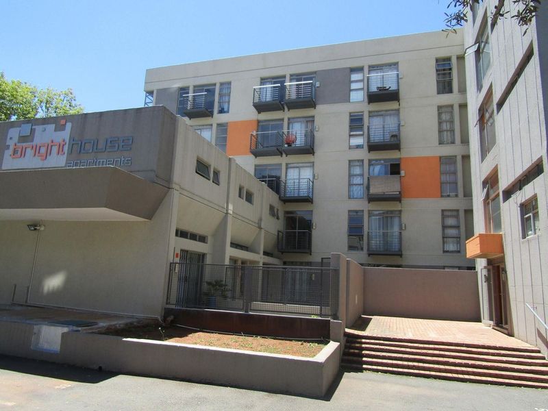 Exterior view of the Bright House apartment complex, featuring a multi-story concrete facade with private balconies and a paved entrance area.
