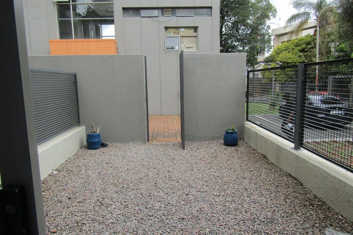 A private, low-maintenance rear courtyard area featuring gravel ground cover, secure metal mesh fencing, and a paved pedestrian access path.