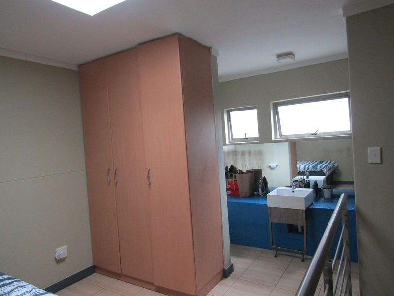 Bedroom featuring a built-in wardrobe, tiled flooring, and an integrated vanity area with a wall-mounted basin and large mirror.