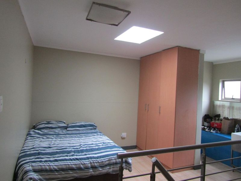 A bedroom featuring built-in cupboards, tiled flooring, and a skylight, with a metal balustrade overlooking the lower level.
