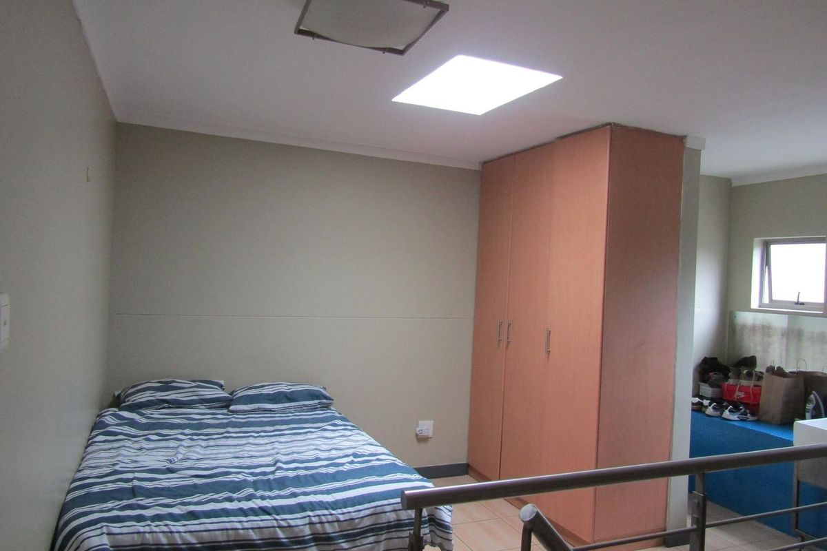 A bedroom featuring built-in cupboards, tiled flooring, and a skylight, with a metal balustrade overlooking the lower level.