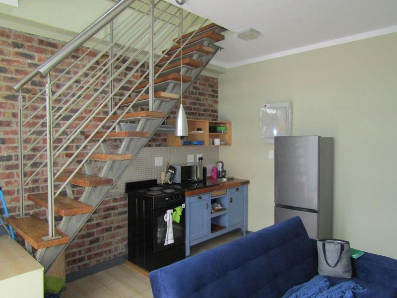 Open plan living area featuring an industrial-style staircase with exposed brickwork and a compact kitchenette with built-in cabinetry.