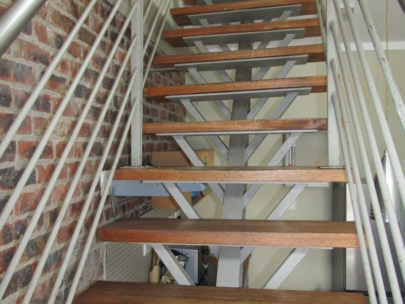 A staircase featuring timber treads, a metal balustrade, and an exposed brick feature wall, providing a modern industrial aesthetic.
