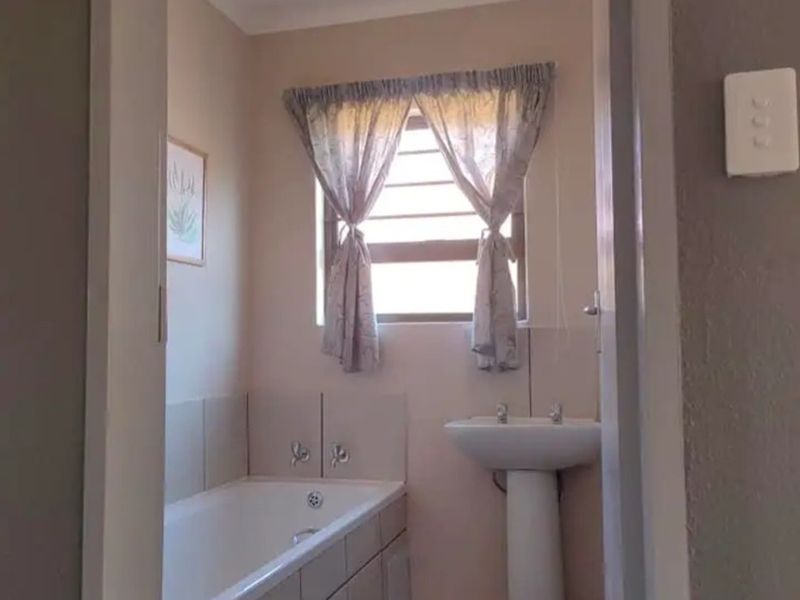A functional bathroom featuring a pedestal basin and a built-in bathtub with tiled surround, offering a clean and neutral space.
