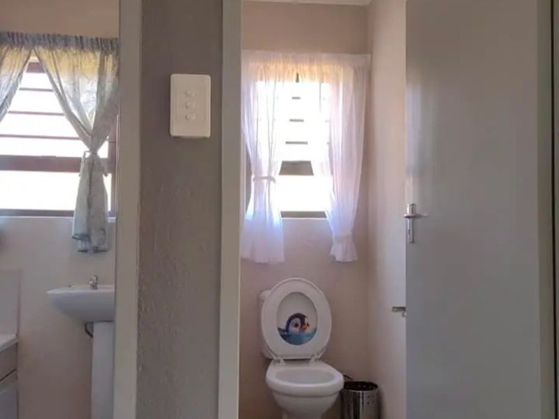 A functional bathroom featuring a pedestal basin and a separate toilet area with louver windows for natural ventilation.