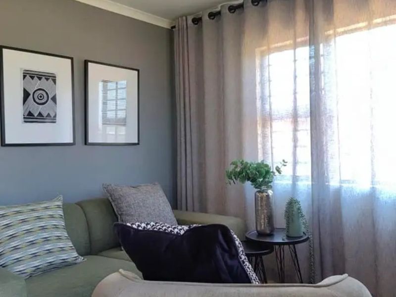 A cozy living room featuring neutral grey walls, a large window with floor-to-ceiling curtains, and classic cove cornicing.