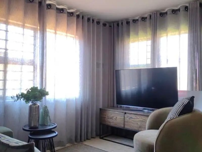 A cozy living room area featuring large windows with floor-to-ceiling curtains, providing ample natural light and a comfortable atmosphere.