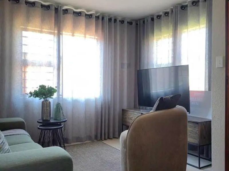 A cozy living room area featuring large windows with installed curtain tracks and neutral wall finishes.
