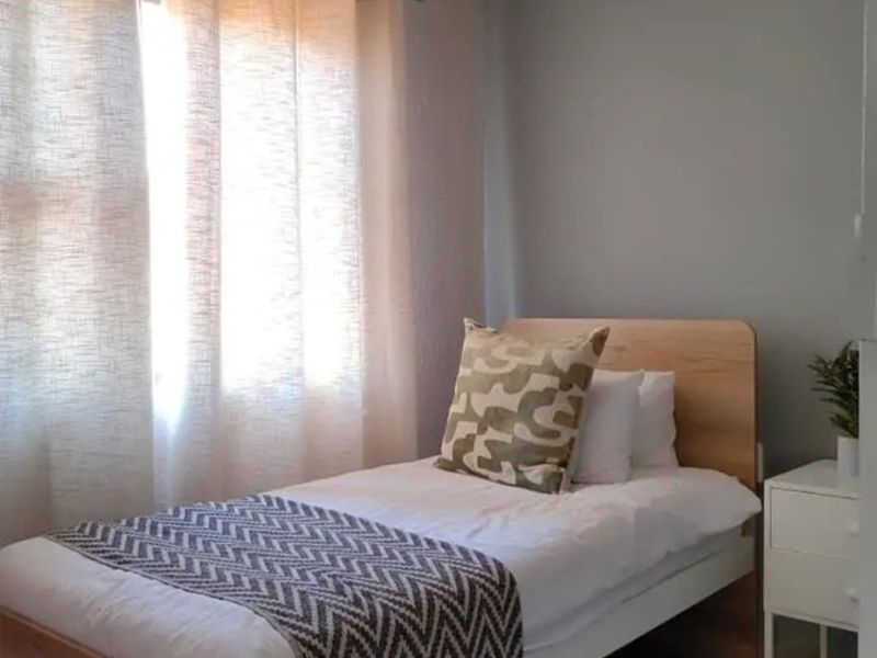 A well-maintained bedroom featuring neutral wall tones, coving, and natural light through window treatments.