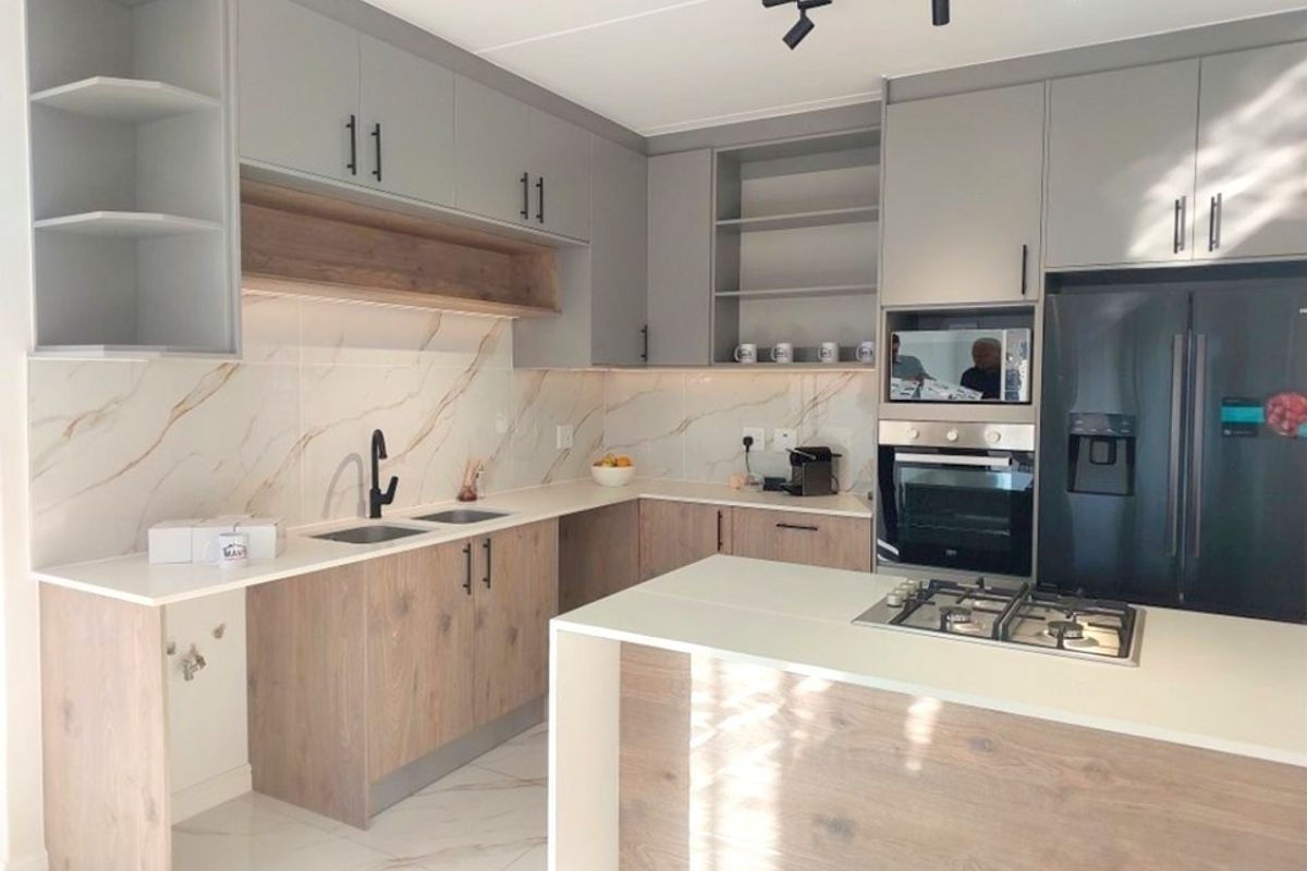 Modern kitchen featuring two-tone cabinetry, stone countertops, marble-look splashback, integrated appliances, and a central island with a gas hob.