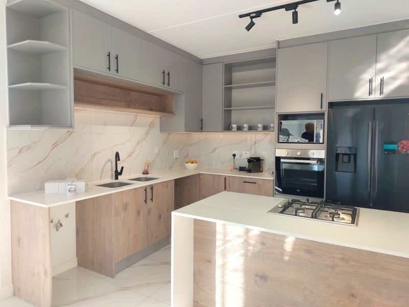Modern kitchen featuring two-tone cabinetry, stone countertops, marble-look splashback, integrated appliances, and a central island with a gas hob.
