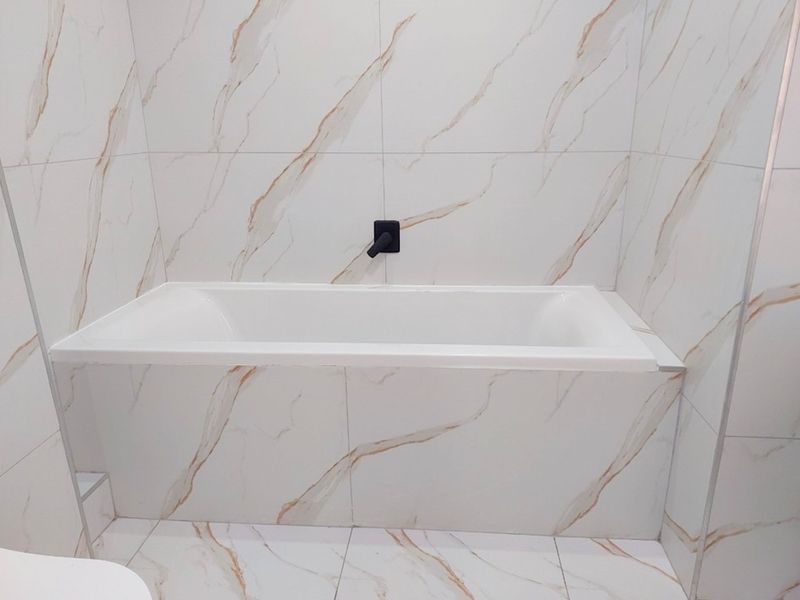 A modern bathroom featuring a built-in bathtub with elegant marble-effect wall and floor tiling and a minimalist wall-mounted mixer tap.