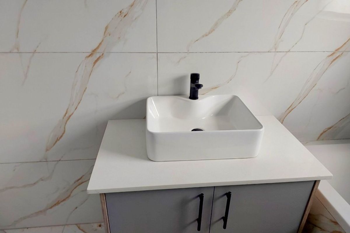 Modern bathroom vanity featuring a white vessel sink, black faucet, and elegant marble-look wall tiling.