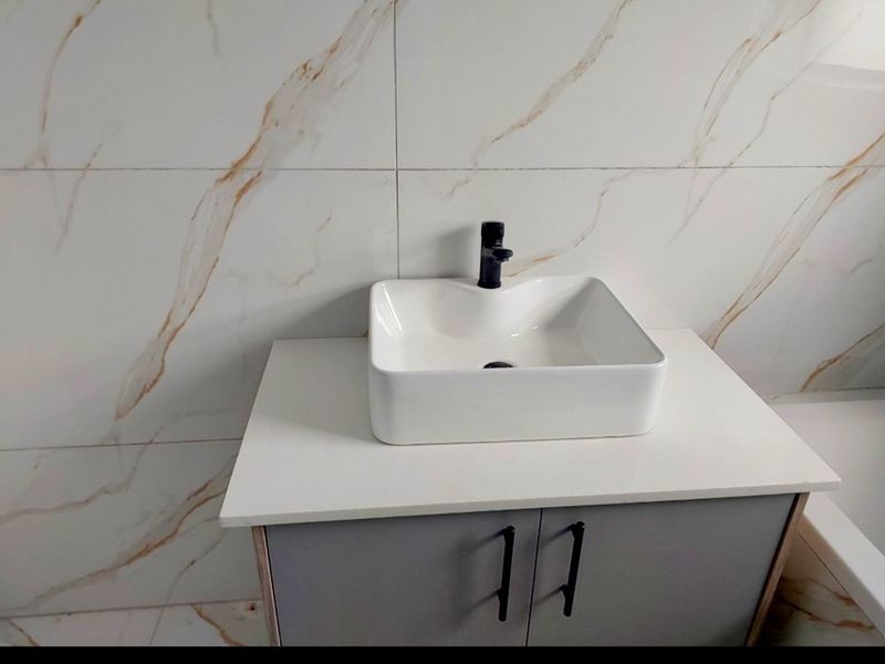 Modern bathroom vanity featuring a white vessel sink, black faucet, and elegant marble-look wall tiling.